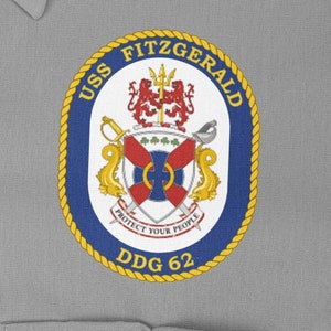 May include: A blue and gold circular patch with the text "USS FITZGERALD DDG 62" and a crest featuring a shield with a cross and a lion.