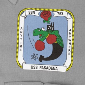 Puede incluir: Un parche azul y amarillo con una tortuga de dibujos animados que lleva guantes de boxeo y un submarino. El parche dice "SSN 752" y "USS PASADENA" con las palabras "ANYTIME" y "ANYWHERE" en los lados.