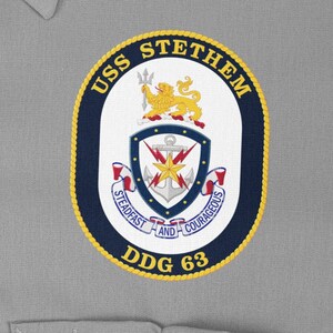 Könnte beinhalten: Gestickter Aufnäher mit dem Wappen der USS STETHEM. Das Wappen hat eine ovale Form mit goldenem Rand, marineblauem Hintergrund und weißer Mitte. Das Wappen enthält einen Dreizack, einen Löwen, einen Anker und den Text "STEADFAST AND COURAGEOUS".