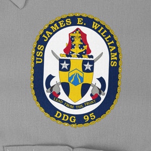 May include: A navy blue and gold circular emblem with the text "USS JAMES E. WILLIAMS" and "DDG 95". The emblem features a shield with a white star and a blue and yellow design. The text "LEAD FROM THE FRONT" is below the shield.