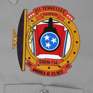 May include: A gold and black circular patch with the text "USS TENNESSEE VOLUNTEERS" and "SSBN-734 AMERICA AT ITS BEST". The patch features a red and blue shield with three white stars and a trident.