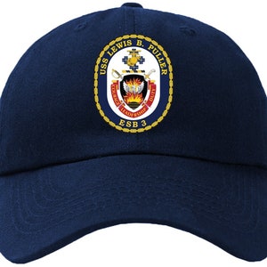 Puede incluir: Una gorra de béisbol azul marino con un parche bordado en oro que presenta el escudo de armas del USS Lewis B. Puller. El escudo incluye un escudo con una espada llameante y las palabras "Valor, Liderazgo, Deber". El texto "USS Lewis B. Puller, ESB 3" también está bordado en el parche.