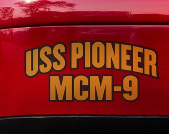 May include: A red car with a gold sticker that says "USS Pioneer MCM-9" on the back bumper.