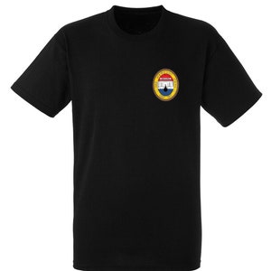 以下が含まれることがあります： 左胸に小さな円形のワッペンが付いた黒いTシャツ。ワッペンは赤、白、青のデザインで、建物と周囲に「The United States of America」という文字が書かれています。
