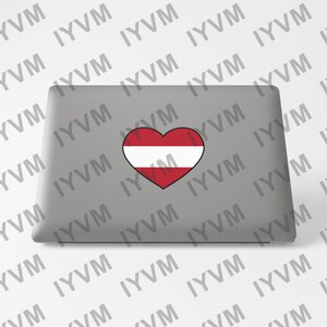 May include: A gray laptop computer with a heart-shaped sticker featuring the Austrian flag. The flag is red, white, and red with a white outline.
