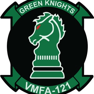 May include: A black and green round patch with a green knight chess piece in the center. The text "GREEN KNIGHTS" is written in a white arc above the chess piece. The text "VMFA-121" is written in a white arc below the chess piece.