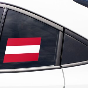 K&ouml;nnte beinhalten: Ein wei&szlig;es Auto mit einem roten und wei&szlig;en Flaggenaufkleber am Heckfenster.