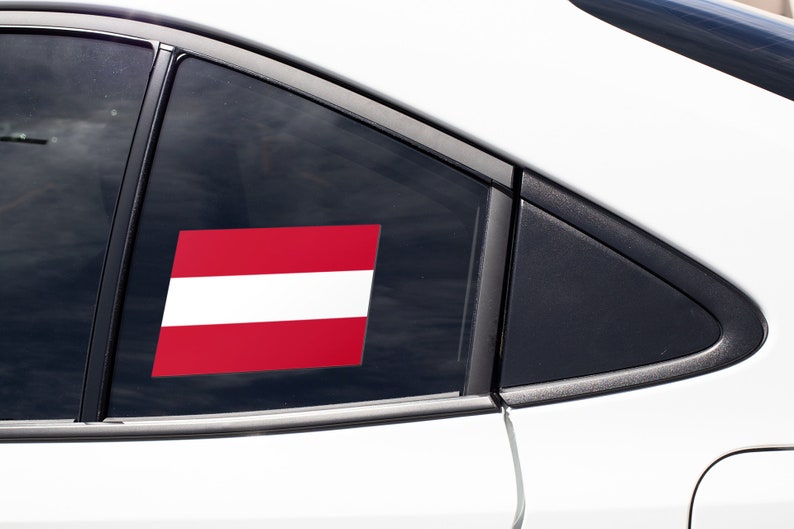 K&ouml;nnte beinhalten: Ein wei&szlig;es Auto mit einem roten und wei&szlig;en Flaggenaufkleber am Heckfenster.