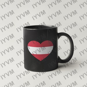 May include: Black ceramic coffee mug with a white heart featuring the Austrian flag. The mug has a white handle.