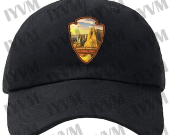 May include: Black baseball cap with a brown patch featuring a scenic image of Theodore Roosevelt National Park. The patch has the text "Theodore Roosevelt National Park" in white.