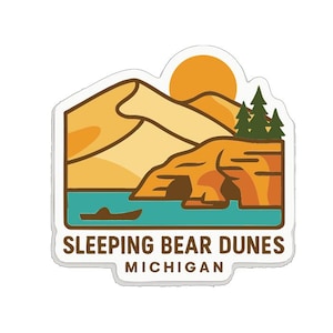 May include: A sticker featuring a landscape design of Sleeping Bear Dunes in Michigan. The design includes a sun, dunes, water, a small boat, and trees. The text "Sleeping Bear Dunes Michigan" is at the bottom.