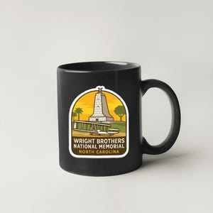 A black coffee mug with a graphic design featuring a monument and text that reads "WRIGHT BROTHERS NATIONAL MEMORIAL NORTH CAROLINA".