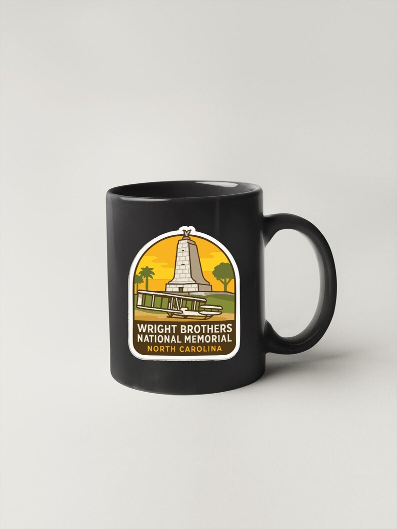 A black coffee mug with a graphic design featuring a monument and text that reads "WRIGHT BROTHERS NATIONAL MEMORIAL NORTH CAROLINA".