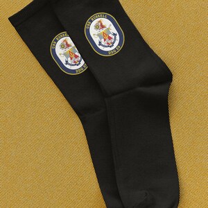 Könnte beinhalten: Ein Paar schwarze Socken mit einem gestickten Aufnäher in Marineblau und Gold mit dem Text "USS RUSSELL DDG 59".