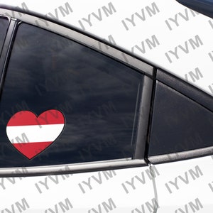 May include: A white car with a heart-shaped sticker on the back window. The sticker is red and white and features the Austrian flag.