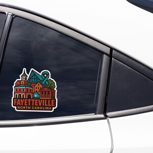 A sticker on the side of a car window, featuring a colorful illustration of a building and the text "FAYETTEVILLE NORTH CAROLINA".