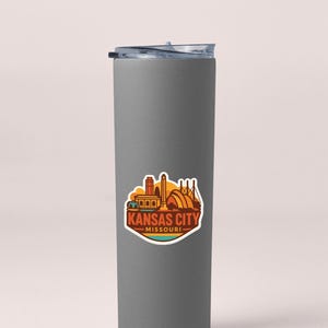 A gray insulated tumbler with a sticker depicting the Kansas City skyline.