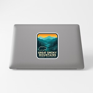 A sticker on the back of a laptop, depicting a scenic mountain landscape with a bear in the foreground.
