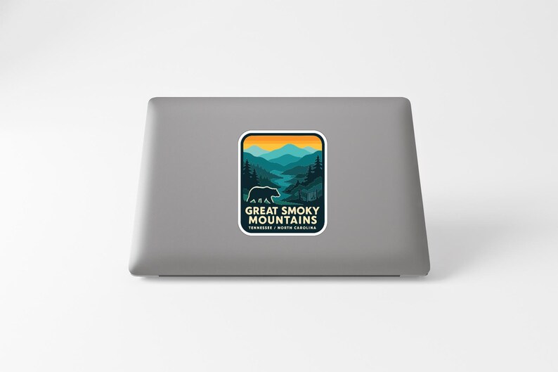 A sticker on the back of a laptop, depicting a scenic mountain landscape with a bear in the foreground.