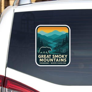 a sticker on the rear window of a vehicle, depicting a scenic mountain landscape with a bear in the foreground.
