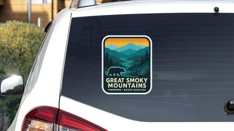 a sticker on the rear window of a vehicle, depicting a scenic mountain landscape with a bear in the foreground.