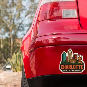the rear end of a red car with a sticker on the trunk that displays the city of Charlotte, North Carolina.