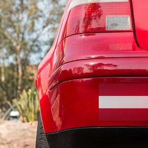 K&ouml;nnte beinhalten: Ein rotes Auto mit einem wei&szlig;en und roten Sto&szlig;f&auml;ngeraufkleber der lettischen Flagge.
