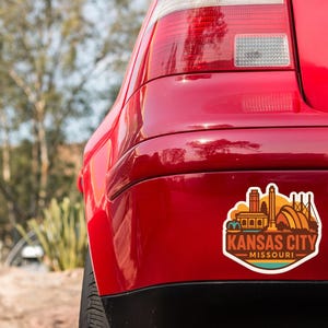 the rear end of a red car with a sticker on the back that says "KANSAS CITY MISSOURI".