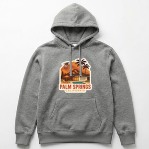 May include: A gray hoodie with a drawstring hood and a kangaroo pocket. The front features a colorful graphic of a desert scene with palm trees and the text "PALM SPRINGS CALIFORNIA".