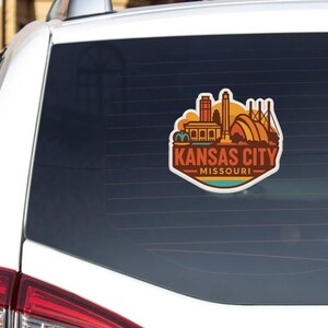 A sticker on the rear window of a white vehicle, depicting the skyline of Kansas City, Missouri.