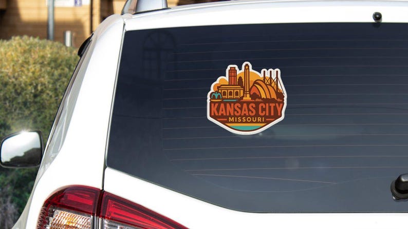 A sticker on the rear window of a white vehicle, depicting the skyline of Kansas City, Missouri.