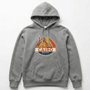 May include: A gray hooded sweatshirt with a front pocket and drawstring. The sweatshirt features a colorful graphic of the Sphinx and pyramids with the text "CAIRO EGYPT" in a badge-like design.