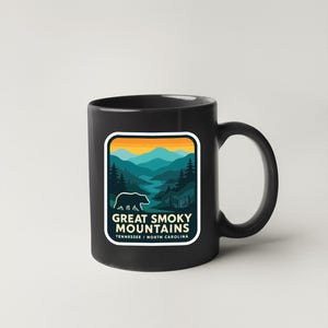 A black coffee mug with a graphic design depicting a mountain landscape and a bear.
