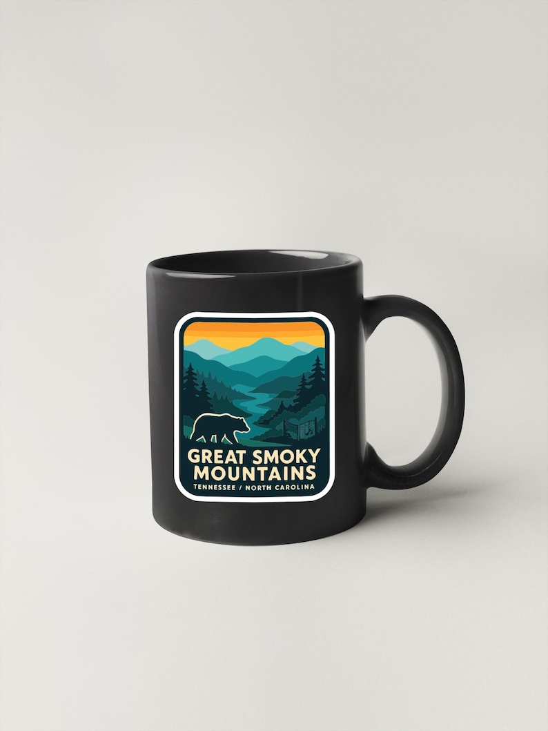A black coffee mug with a graphic design depicting a mountain landscape and a bear.