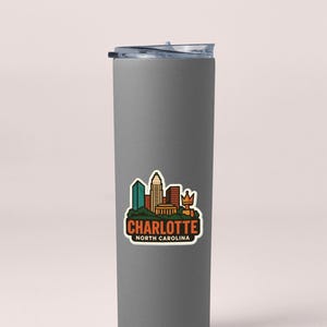 A gray insulated tumbler with a printed sticker depicting the skyline of Charlotte, North Carolina.