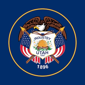 Puede incluir: La bandera oficial del estado de Utah, con un fondo azul y un círculo dorado en el centro. El círculo contiene un águila calva con las alas extendidas, sosteniendo flechas en sus garras. Debajo del águila hay un escudo con las palabras "Industry", "Utah" y "1847". El escudo está flanqueado por dos banderas americanas cruzadas. El año "1896" está impreso debajo del escudo.