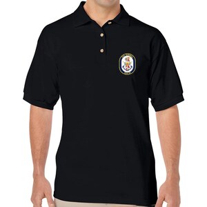 Könnte beinhalten: Schwarzes Poloshirt mit einem marineblauen gestickten Aufnäher mit einem Wappen und dem Text "USS RIGEL  DDG 99"