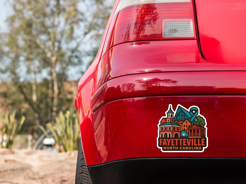 the rear end of a red car with a sticker on the trunk that features a colorful illustration of a cityscape.