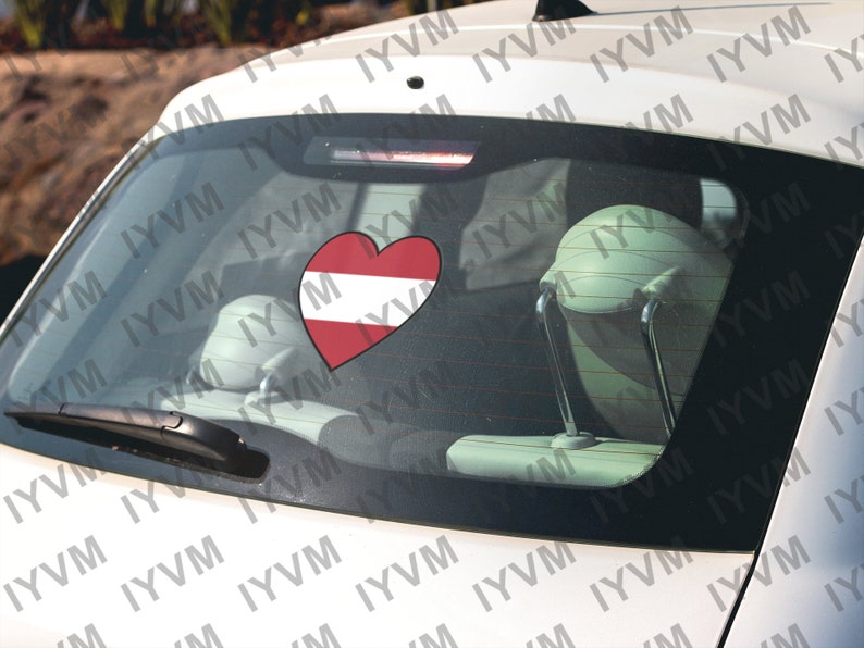 May include: A white car with a red heart sticker on the back window. The heart is decorated with the colors of the Austrian flag.