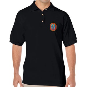 Könnte beinhalten: Schwarzes Poloshirt mit einem kleinen gestickten Aufnäher auf der linken Brust. Der Aufnäher ist rot, weiß und blau und zeigt eine Rakete mit dem Text "United States Space Force".