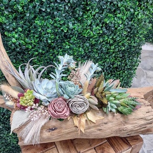 May include: A rustic wooden log centerpiece with a variety of succulents, air plants, and dried flowers. The centerpiece is decorated with dried grasses and feathers.