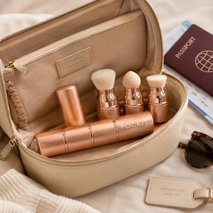 May include: A beige cosmetic travel case containing a rose gold modular brush set with the text POCKIT LONDON printed on the handle. The case features an interior pocket with the embossed text TAKE BEAUTY ANYWHERE and includes a passport and luggage tag.