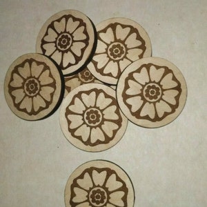 Op de afbeelding: Een verzameling houten onderzetters met een lasergeëtst bloemmotief. De onderzetters zijn rond, met een lichte houtkleur en een donkerder bruin bloemmotief. Het ontwerp heeft een centrale cirkel omgeven door hartvormige bloemblaadjes.