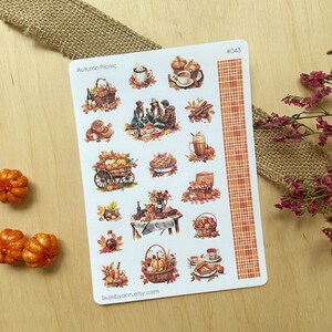 Op de afbeelding: Een vel stickers met een herfstpicknickthema. De stickers bevatten illustraties van herfstbladeren, eten en mensen die genieten van een picknick. De stickers zijn op een witte achtergrond met een rood-wit geruite rand. De tekst "Autumn Picnic" en "#043" staat op het vel gedrukt.