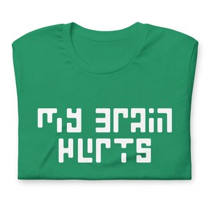 May include: A folded, green t-shirt with the white text "MY BRAIN HURTS" in a blocky, pixelated font. The shirt is made of a soft material and has a classic crew neck design.