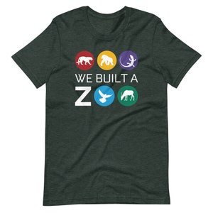 May include: A dark green t-shirt with a white graphic that says "WE BUILT A ZOO" with five colorful circles featuring animal silhouettes. The circles feature a leopard, gorilla, lizard, dove, and antelope.