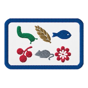 Puede incluir: Parche bordado con fondo blanco y borde azul. El parche presenta imágenes bordadas de un gusano verde, una hoja marrón, un pez azul, cerezas rojas, un ratón gris y una flor roja y blanca.