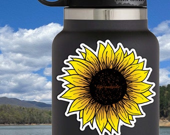 May include: A yellow sunflower sticker with a black center and white outline. The sticker is on a black water bottle with the text "Life Outside Sticker Company" on the top. The sticker is 3 inches by 3 inches.
