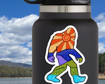 May include: A colorful sticker of a Bigfoot walking with a sun rising behind it. The sticker is 3 inches by 1.75 inches. The sticker is on a black water bottle with the text "Life Outside Sticker Company".