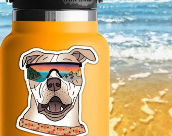 May include: A white dog with brown ears wearing sunglasses with a sunset reflection. The dog is wearing a colorful patterned bandana. The sticker is 2.5 inches by 2 inches.  Life Outside Sticker Company.